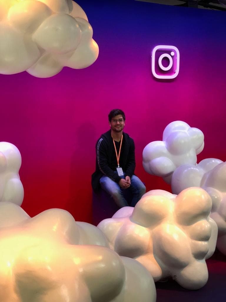 Matheus Siqueira in a black jacket, seated among white cloud sculptures, with the Instagram neon logo behind him.