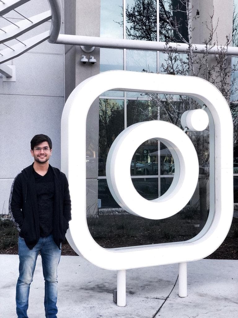Matheus Siqueira beside a large white Instagram logo sculpture in front of a glass building.
