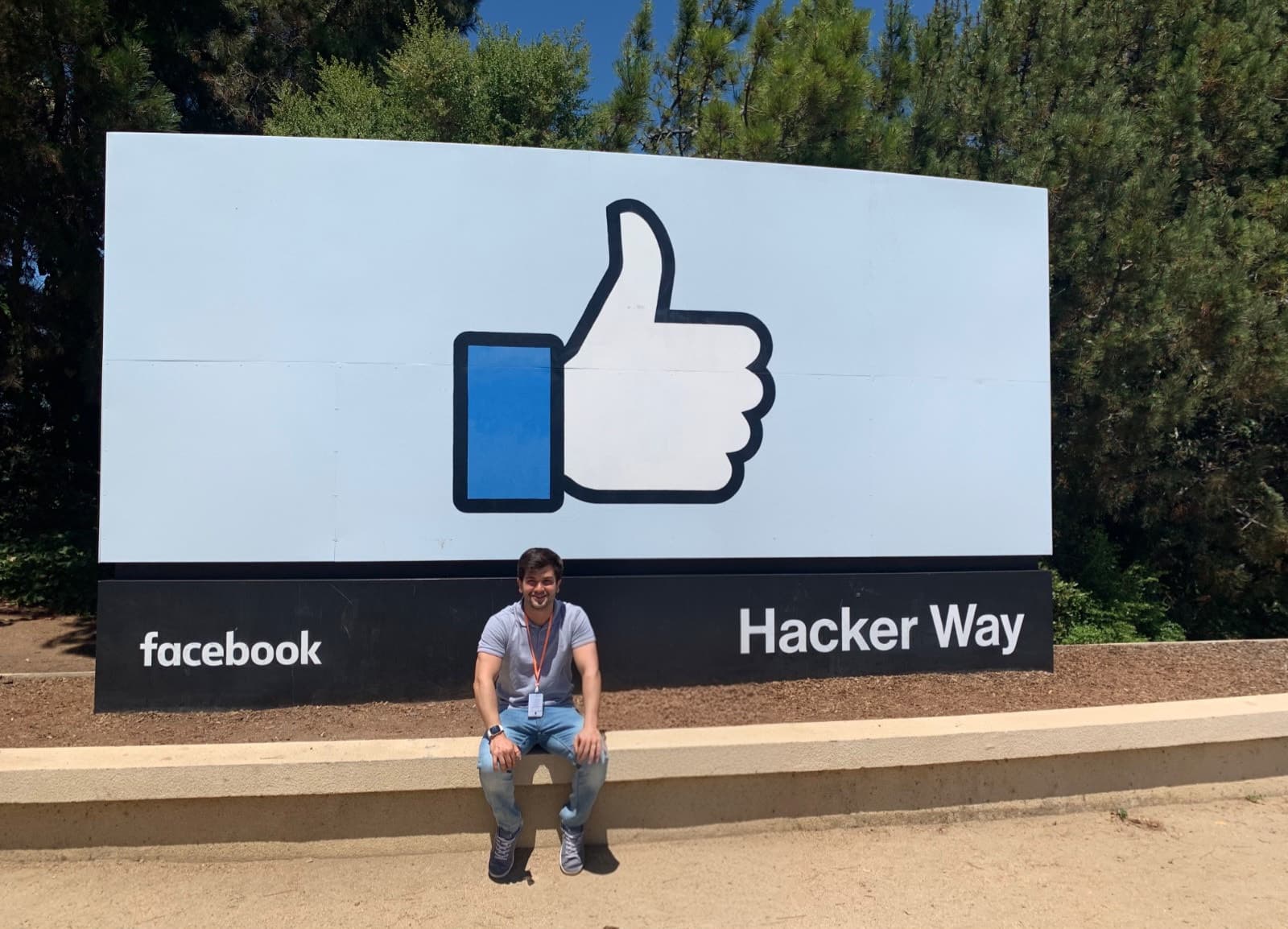 Matheus Siqueira seated in front of the Facebook sign with the like symbol and the name Hacker Way.